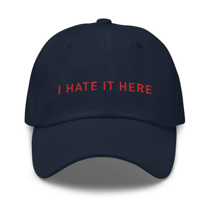 Bild eines Baseball-Caps mit dem Spruch 'I HATE IT HERE' auf weißem Hintergrund. Ein humorvolles Accessoire für diejenigen, die lieber zuhause bleiben. Hergestellt aus Baumwoll-Chino-Cord.